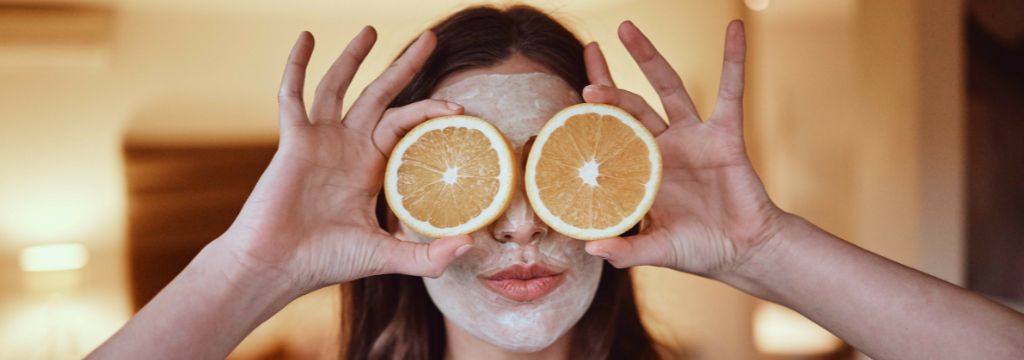 Jovem branca segura duas metades de laranja na frente dos olhos enquanto posa para a foto